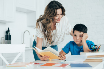 Fototapeta premium portrait of mother helping bored son with homework at home