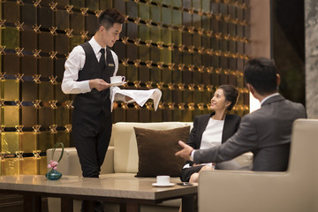 Young waiter serving coffee to business people