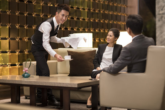 Young waiter serving coffee to business people