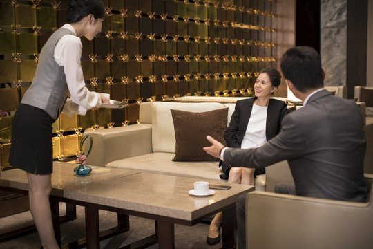 Young waitress serving coffee to business people