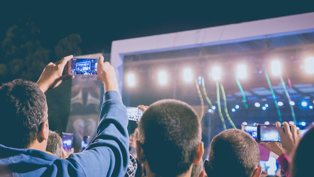 A group of young man recording music event by their mobile phone cameras