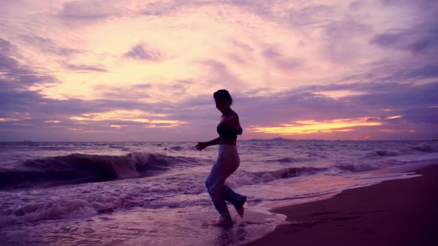 Silhouette attractive young asian woman with sunglasses dancing on beach on beautiful windy with twilight in sunset,Slow motion footage
