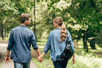 rear view of beautiful young couple in denim shirts walking by park - Powered by Adobe