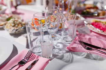 Glasses, forks, knives, napkins and a decorative flower on a white tablecloth table are served for dinner in a cozy restaurant. Decorated table for a wedding or a party.