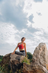 Fresh air. Woman wearing comfortable sport clothes enjoying fresh air while stretching near rocks