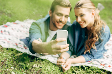 beautiful young couple lying on grass at park and taking selfie