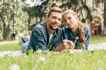 Naklejka na ściany i meble happy young couple lying on grass at park and looking at camera