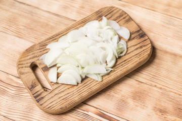 Sliced onions with half rings on a wooden chopping board on a wooden background.