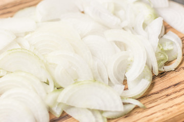 Sliced onions with half rings on a wooden chopping board on a wooden background.