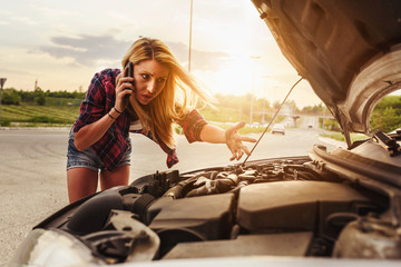 Attractive blonde in front of her car broken down car, assistance concept. Upset woman emotionally reacting on overheated car standing on the roadside with the open hood.