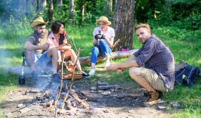 Naklejka na ściany i meble Hikers sit near campfire relaxing while wait roasting food. Hikers organized quick picnic to eat and relax. Hikers spend leisure in forest nature background. Youth hiking vacation. Hike picnic ideas