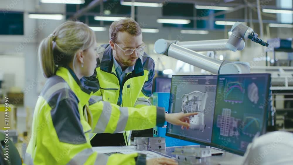 Poster At the Factory: Male Mechanical Engineer Holds Component and Female Chief Engineer Work on Personal Computer, They Discuss Details of the 3D Engine Model Design for Robotic Arm.
