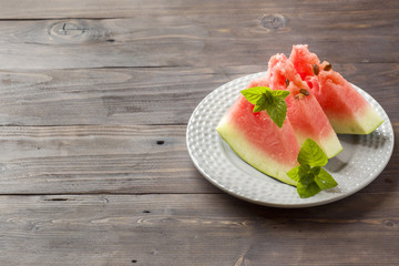 Watermelon sliced on a plate with mint leaves on a wooden background. Copy space