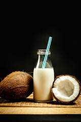 fresh brown coconuts and bottle of milk on a wooden table on a black background