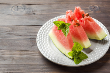 Watermelon sliced on a plate with mint leaves on a wooden background. Copy space