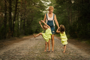 Naklejka na ściany i meble beautiful mother and two adorable daughters in dresses posing on the road in the summer forest