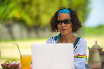 lifestyle outdoors portrait of young happy and attractive afro american mixed ethnicity woman working with laptop computer from beautiful cafe