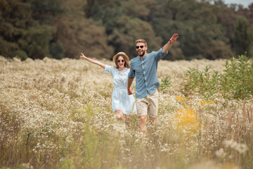happy lovers holding hands while running in field with wild flowers