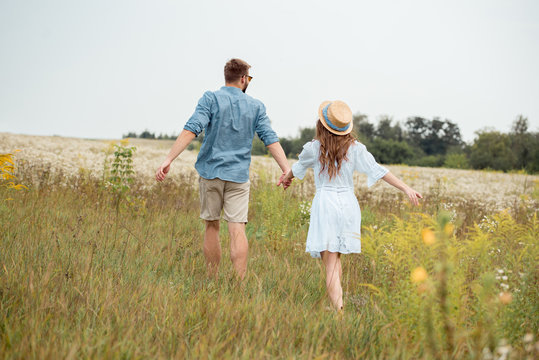 back view of young lovers holding hands while running in field with wild flowers - Powered by Adobe