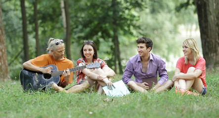 Fototapeta premium group of students sing songs sitting on the lawn in the city Park