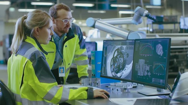 At the Factory: Male Mechanical Engineer and Female Chief Engineer Work Together on the Personal Computer, They Discuss Details of the 3D Engine Model for Robotic Arm.