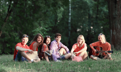 group of friends students with books and guitar sitting on the grass in the Park