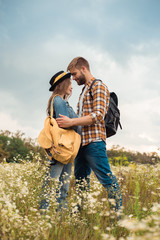 tender couple in love with backpacks in summer field with wild flowers