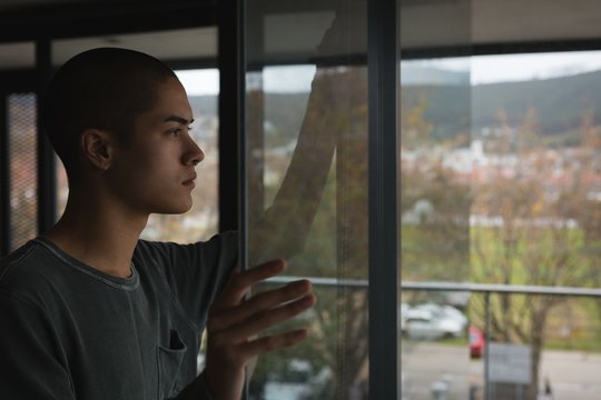 Androgynous young man looking through window at home