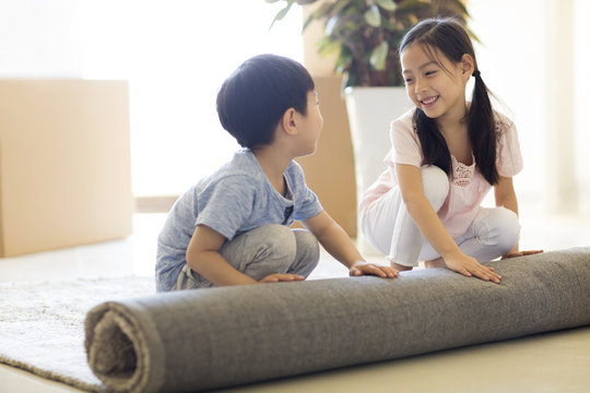 Cute children unrolling carpet in new house