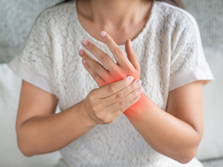 Closeup young woman sitting on sofa holds her wrist. hand injury, feeling pain. Health care and...