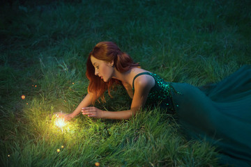 red hair charming woman is lying on the grass in a wonderful emerald dress with long train