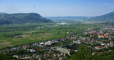 Colorful exalted view from a bird's eye view to houses in residential district in the city of Khust, Western Ukraine with high mountains in the background on a background of green vegetation.