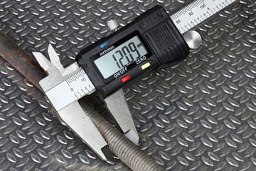 Measurement of a threaded steel rod with digital caliper over corrugated metal background