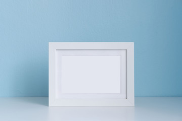 blank white picture frame on the table with blue background