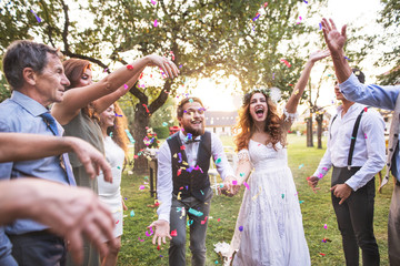 Bride, groom and guests throwing confetti at wedding reception outside. - Powered by Adobe