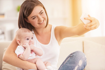 Happy Mother Using Smartphone and Holding Baby.