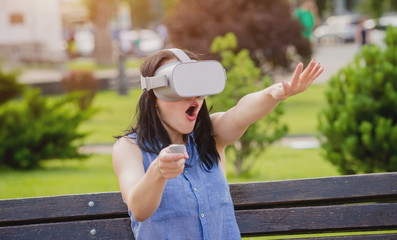 A beautiful young girl plays a game wearing virtual reality glasses on the street.