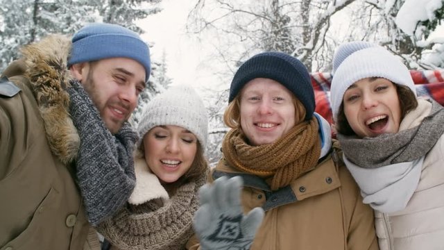 Company of young happy friends smiling, yelling and waving at camera while spending winter day outdoors