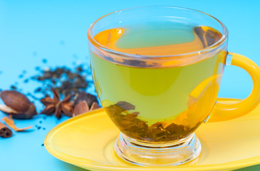 Hot cup of spicy lemon tea or infusion in an elegant yellow glass cup and saucer with spice ingredients behind