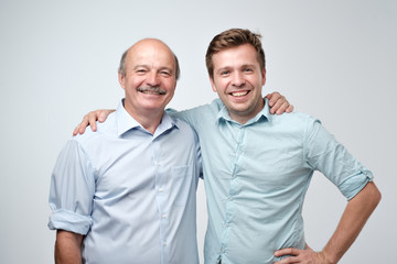 Hispanic father and adult son hugging and smiling at camera.