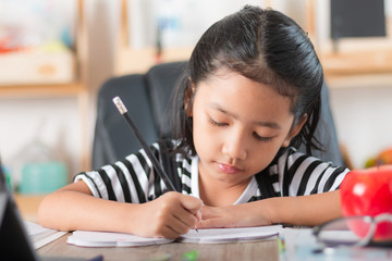 Asian little girl doing homework and pointing finger on wooden table select focus shallow depth of field