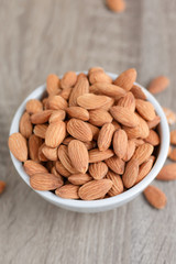 Pile of almonds nut in a while bowl against wooden background select focus shallow depth of field