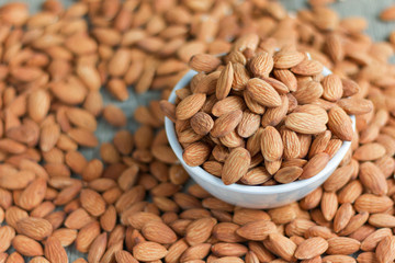 Pile of almonds nut in a while bowl against wooden background select focus shallow depth of field