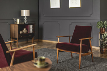 Burgundy armchair placed on dark carpet in grey living room interior with blurred foreground