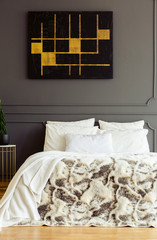 Black and gold poster on the wall above patterned bed in grey bedroom interior. Real photo