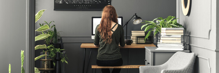 Panorama of a girl student sitting on a wooden bench by an industrial desk with a computer in a...
