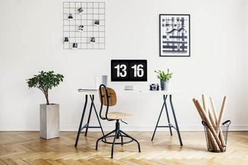 Real photo of a simple home office interior with a desk, chair, plant, computer, poster and wall...