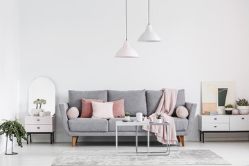 Real photo of an elegant living room interior with a grey sofa, pink pillows, cabinets and lamps