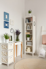 Real photo of wooden rack with books and decor, posters on wall and lavender in glass vase standing on console table