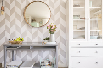Mirror on patterned wallpaper above grey table with flowers in s